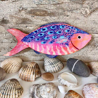 Large wooden fish decoration by Lee Foster-Wilson displayed on real shells against a stone wall