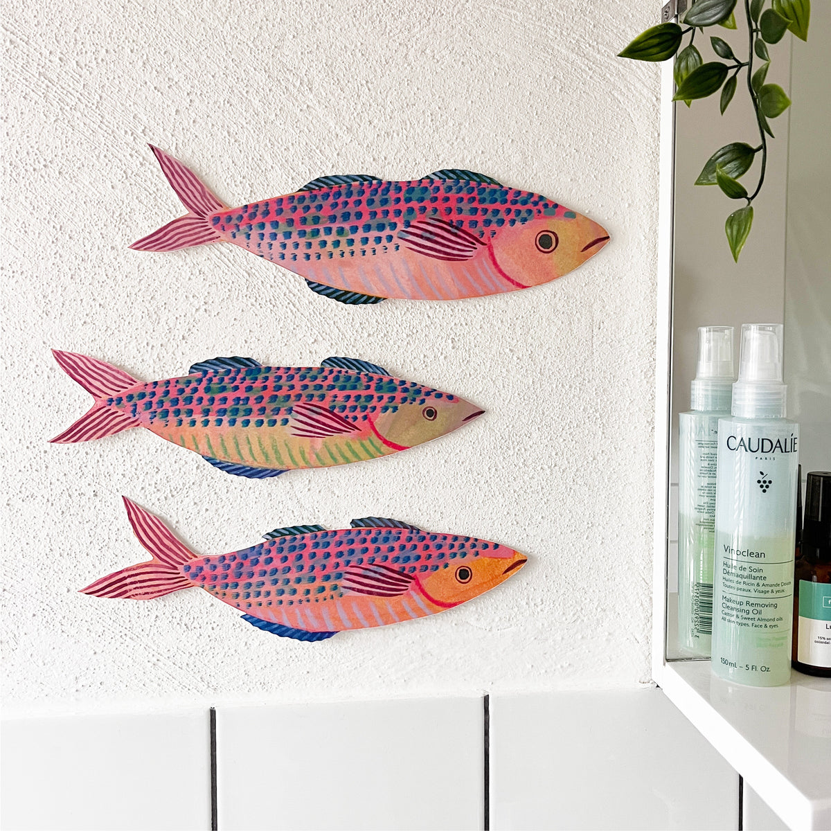 Colourful mackerel fish decorations by Lee Foster-Wilson displayed on a rough textured wall next to a bathroom mirror