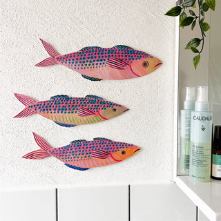 Colourful mackerel fish decorations by Lee Foster-Wilson displayed on a rough textured wall next to a bathroom mirror