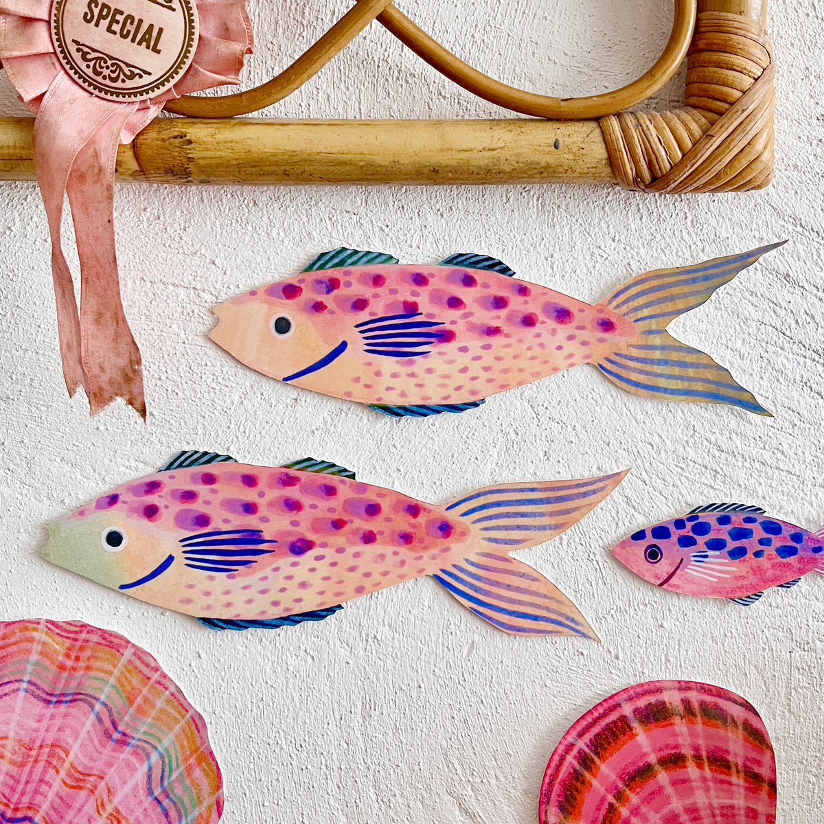Colourful fish decorations by Lee Foster-Wilson displayed on a rough textured wall beneath a rattan frame